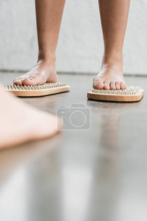 cropped view of barefoot woman with tattoo standing on sadhu nail board in yoga studio 