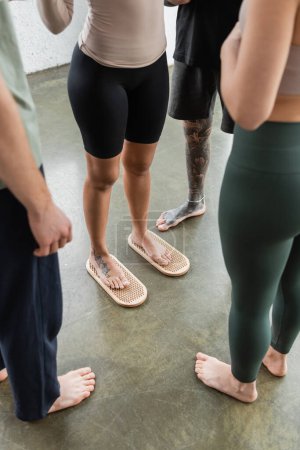 Téléchargez les photos : Vue recadrée d'une femme tatouée debout sur une planche à ongles sadhu près de personnes dans un studio de yoga - en image libre de droit