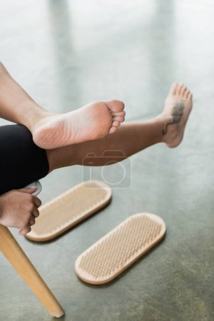 Foto de Vista parcial de la mujer tatuada mostrando los pies desnudos después de la práctica de pie clavo en el estudio de yoga - Imagen libre de derechos
