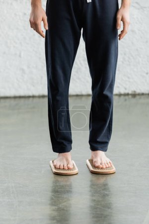 Teilaufnahme eines barfüßigen Mannes in Hose, der auf einem Sadhu-Brett im Yogastudio steht 