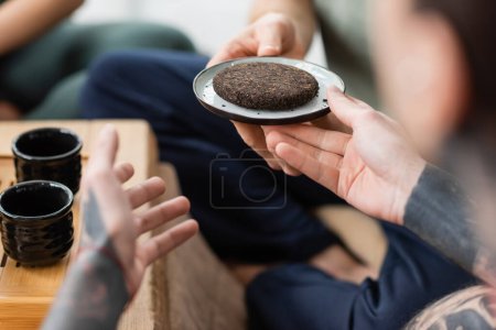 Foto de Vista recortada del hombre tatuado tomando plato con té puer comprimido y fermentado - Imagen libre de derechos