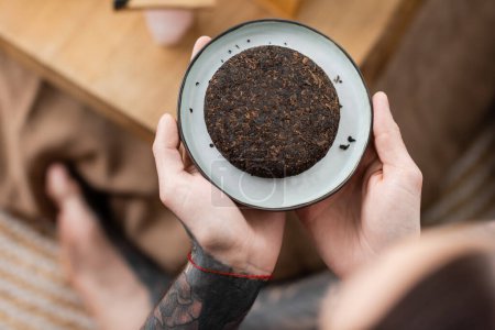 top view of tattooed man holding plate with compressed chinese puer tea 