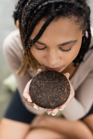 top view of african american woman with dreadlocks smelling compressed puer tea