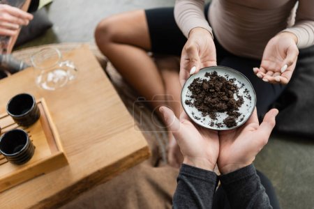 top view of african american woman passing plate with fermented puer tea to man in yoga studio 