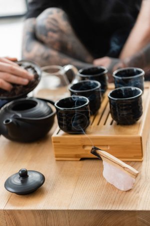 Téléchargez les photos : Brûlant Palo Santo bâton près de l'homme en ajoutant du thé puer dans la théière chinoise traditionnelle dans le studio de yoga - en image libre de droit