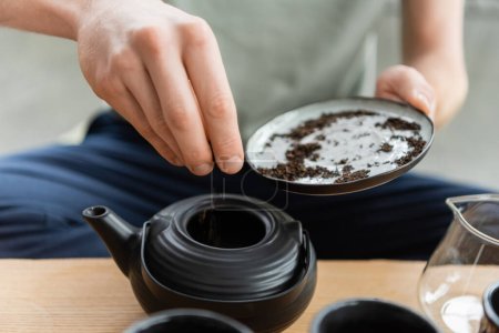 cropped view of man adding dried puer tea leaves in Chinese tea pot 