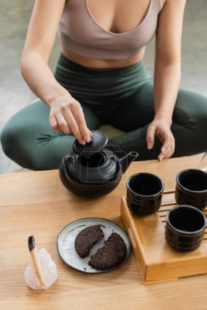 Foto de Vista recortada de la mujer en ropa deportiva elaboración de té puer en tetera china - Imagen libre de derechos
