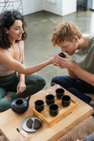 curly middle eastern woman smiling while giving to smell puer tea to redhead man 
