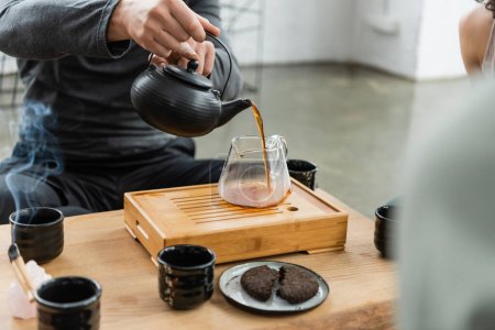 cropped view of man pouring freshly brewed puer tea into glass jug 