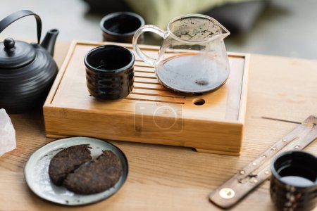 komprimierter Pu-Erh-Tee in der Nähe chinesischer Teekanne und Räucherstäbchen auf Holzständer 