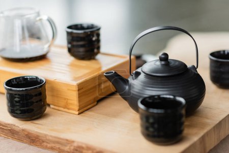 tradycyjny japoński czajniczek w pobliżu filiżanek i szklany dzbanek z czystą herbatą na rozmytym tle 