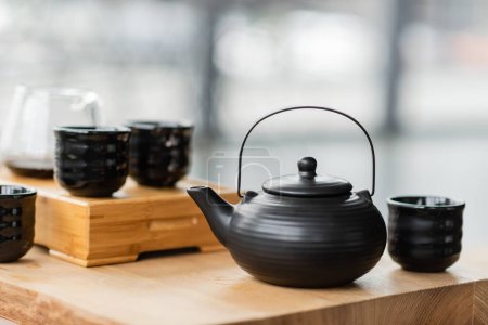 Traditionelle chinesische Teekanne in der Nähe von Tassen und Glaskanne mit Puertee auf verschwommenem Hintergrund 