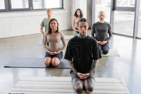 Interracial group of people meditating with closed eyes in Thunderbolt yoga pose 