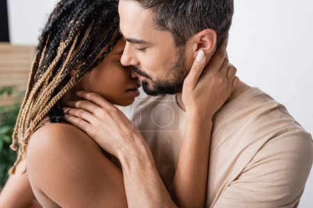 Téléchargez les photos : Vue latérale de l'homme barbu brune et femme américaine africaine chaude avec dreadlocks baisers à la maison - en image libre de droit