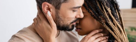 Photo for Side view of bearded man and young african american woman with dreadlocks kissing at home, banner - Royalty Free Image