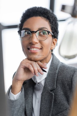Téléchargez les photos : Portrait de femme d'affaires afro-américaine heureuse et réussie dans des lunettes élégantes regardant loin dans le bureau - en image libre de droit