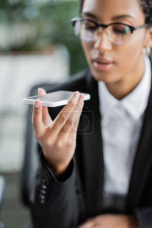 blurred african american businesswoman recording voice message on cellphone in office