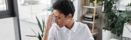 exhausted african american businesswoman touching forehead while suffering from headache in office, banner