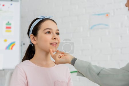 Speech therapist touching chin of preteen pupil during lesson in consulting room 