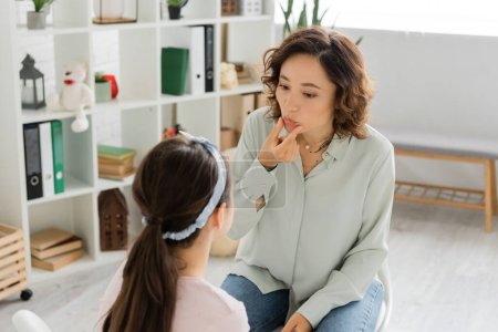 Speech therapist touching mouth during lesson with child in consulting room 