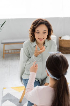Speech therapist sticking out tongue near blurred preteen child in consulting room 