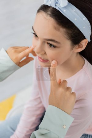 High angle view of speech therapist touching cheeks of pupil in consulting room 