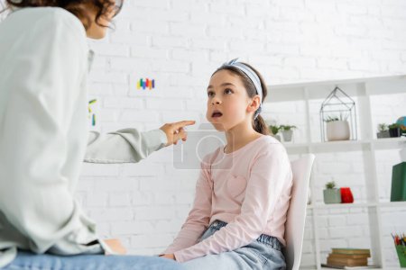 Speech therapist pointing at cheek of preteen girl in consulting room 
