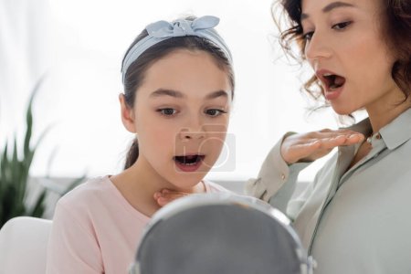 Logopädin und Kind reden im Sprechzimmer in der Nähe eines verschwommenen Spiegels 