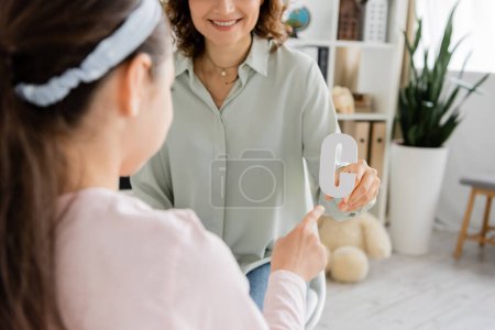 Smiling speech therapist holding letter c while blurred kid pointing with finger in consulting room 