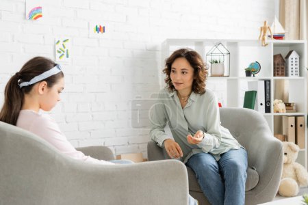 Psychologist talking to displeased preteen girl in consulting room 