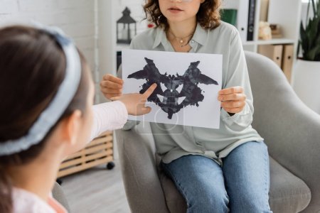 Blurred girl pointing at Rorschach test near psychologist in consulting room 