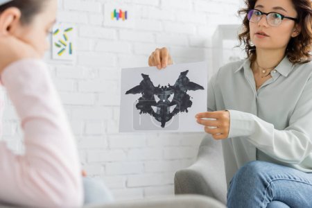Psicólogo sosteniendo prueba de Rorschach cerca borrosa niña preadolescente en la sala de consulta 