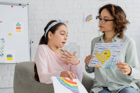 Preteen child talking while psychologist holding drawing in consulting room 