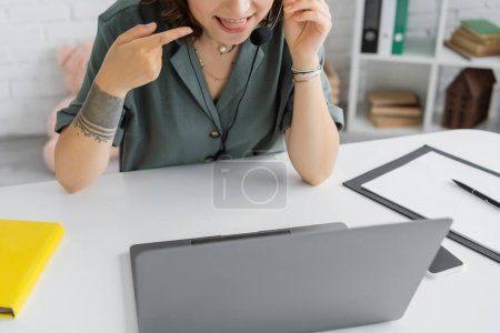 Cropped view of speech therapist pointing at tongue during video call on laptop in consulting room 