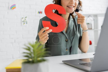 Photo for Cropped view of smiling speech therapist in headset holding letter s during video call on laptop - Royalty Free Image