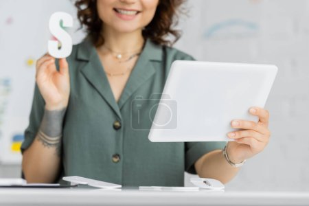 Vista recortada del terapeuta del habla borroso sosteniendo las letras s durante la lección en línea en la sala de consulta 