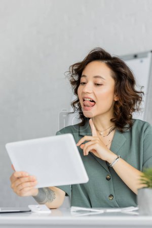 Speech therapist pointing at tongue during online lesson in consulting room 