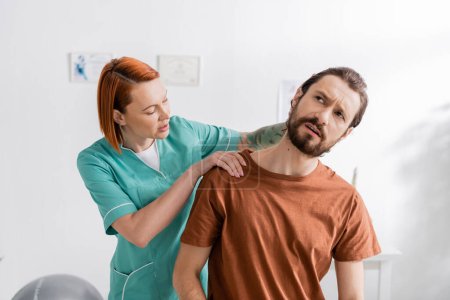 Photo for Rehabilitation specialist examining painful neck of bearded man during appointment in consulting room - Royalty Free Image
