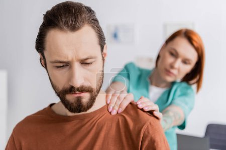 Photo for Blurred chiropractor touching painful shoulder of bearded man during diagnostics in hospital - Royalty Free Image