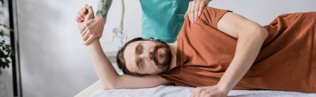 Téléchargez les photos : Homme barbu avec les yeux fermés près physiothérapeute faire massage soulagement de la douleur dans la salle de consultation, bannière - en image libre de droit