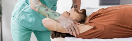 terapeuta manual tatuado haciendo masaje de alivio del dolor al hombre lesionado en el centro de rehabilitación, pancarta