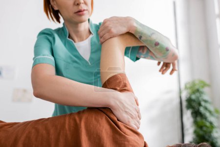 Teilansicht des manuellen Therapeuten beugt schmerzhaften Arm des Mannes in Reha-Zentrum