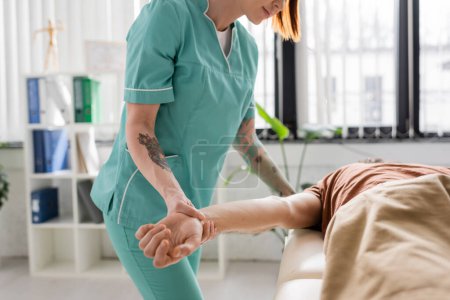 partial view of manual therapist massaging injured arm of man in hospital