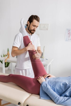 Physiotherapeut streckt Bein einer Frau während Schmerztherapie im Reha-Zentrum