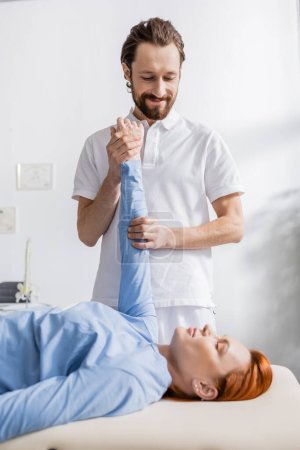 Lächelnder Physiotherapeut streckt Arm der Frau, während er Schmerzlinderungs-Massage im Erholungszentrum macht