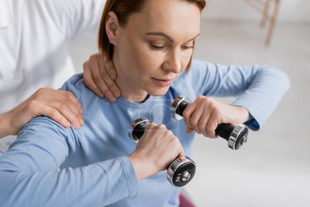 woman training with dumbbells near physiotherapist in rehabilitation center
