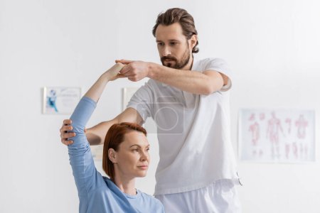 Téléchargez les photos : Physiothérapeute barbu bras de soutien de la rousse femme exerçant dans le centre de réadaptation - en image libre de droit