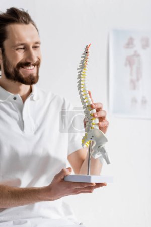 pleased bearded osteopath looking at spine model in consulting room