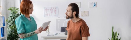 tattooed physiotherapist with digital tablet talking to bearded man in consulting room, banner