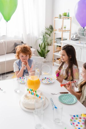 Blick aus der Vogelperspektive auf fröhliche Kinder mit Partyhörnern zum Geburtstag zu Hause 